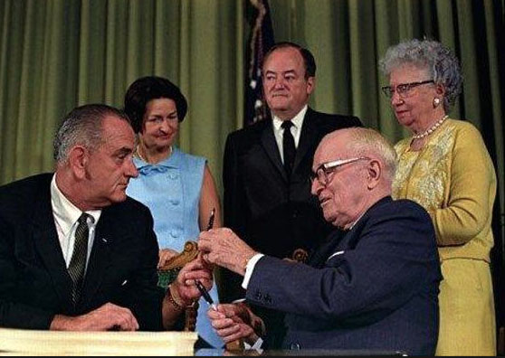Harry and Bess Truman watch with Lady Bird Johnson as President Lyndon B. Johnson signs the Medicare Act, and made the elderly couple the first two recipients of the federal medical coverage. (LBJ Library)